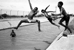 Juhan Kuus. Esimene koolipäev ja 33 kraadi sooja. Bridgtoni linnakese lapsed jahutavad end kuivenduskraavis tapamaja lähistel.  Lõuna-Aafrika, 8. XII 2003.